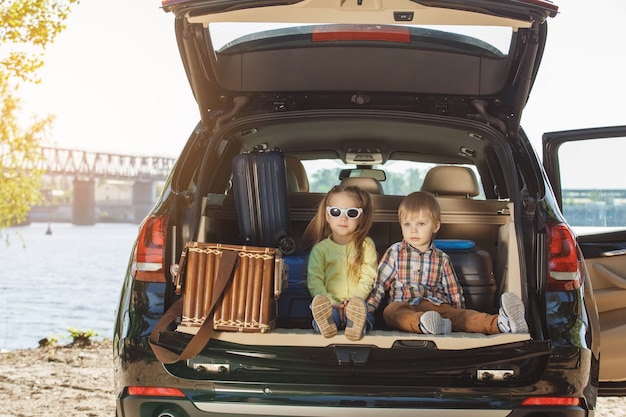 Foto viagem de carro, família, irmão e irmã sentados em um porta-malas