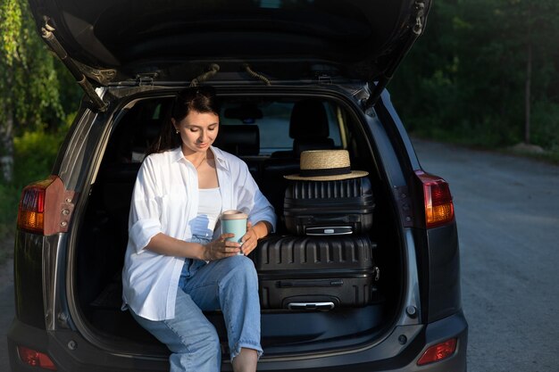 Viagem de carro Uma jovem linda de chapéu de férias descansa perto do carro Estilo de vida