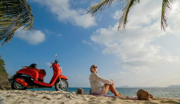 Viagem de scooter Mulher sozinha na moto vermelha em roupas brancas na praia de areia pelo oceano