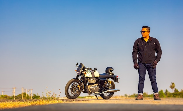 Viagem de verão em uma motocicleta, motorista de motocicleta com jaqueta de couro preta está na estrada com a motocicleta vintage estendida, foco seletivo