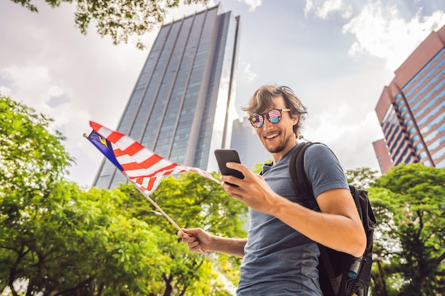 Viagem e tecnologia Jovem turista com a bandeira da Malásia está olhando para um mapa da cidade em um smartphone para navegação