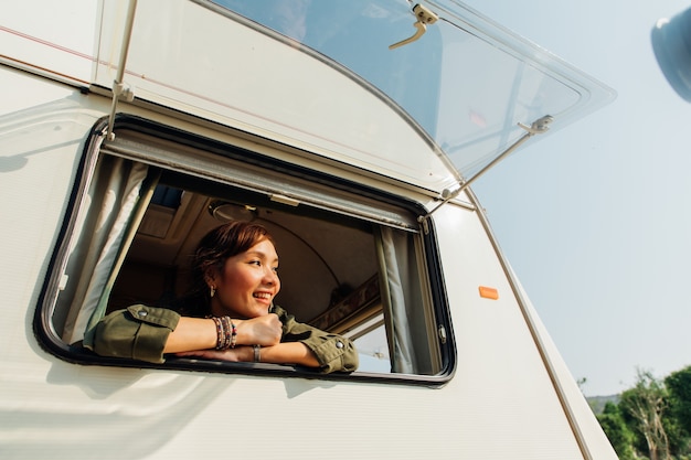 Viagem em família de carro de caravana em belas férias. Jovem mulher asiática em caravana com uma xícara de café branca de manhã