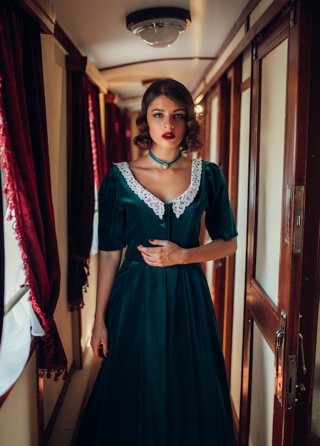 Viagem ferroviária, mulher em vestido retrô, interior de compartimento de trem vintage.