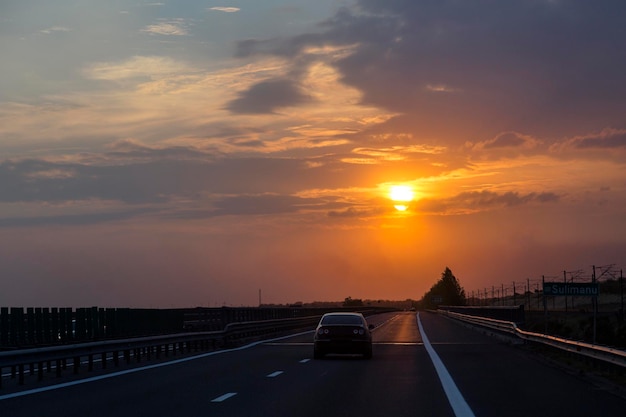 Viagem por estrada no céu laranja do pôr do sol à noite um carro na estrada