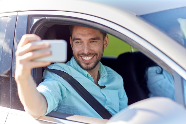 viagem, transporte, viagens, tecnologia e conceito de pessoas - homem sorridente feliz com smartphone dirigindo no carro e tirando selfie