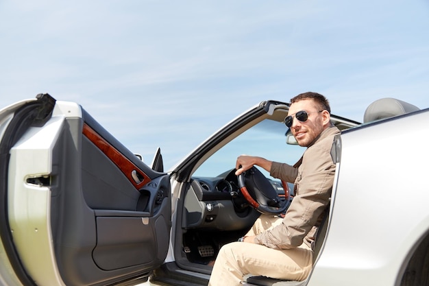 viagem, viagens, transporte, lazer e conceito de pessoas - homem feliz abrindo a porta do carro cabriolet ao ar livre