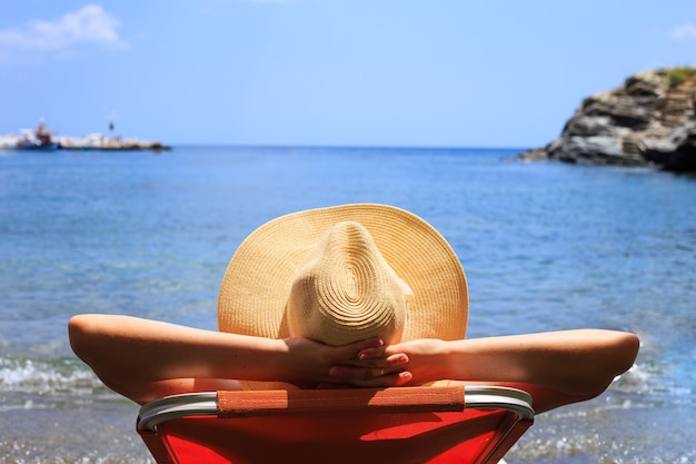 Viagem, vocação, conceito de férias. Mulher de chapéu está deitada na espreguiçadeira na praia, à beira-mar.