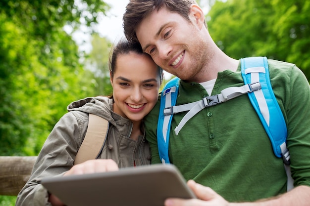 viagens, caminhadas, mochila, turismo e conceito de pessoas - casal sorridente com mochilas e computador tablet pc na natureza