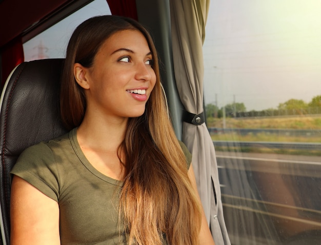 Viagens fáceis. garota viajante usando ônibus confortável para se mover. jovem e bela mulher olhando pela janela do ônibus. passageiro de ônibus feliz viajando sentado em um assento e olhando pela janela.