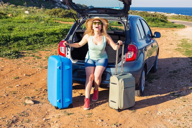 Viagens, férias de verão e conceito de férias - jovem mulher com malas em viagem de carro.