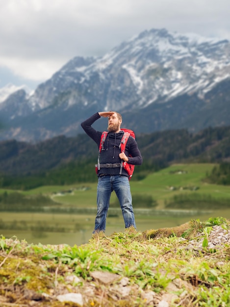 viagens, turismo, caminhada e conceito de pessoas - turista com barba, mochila em pé na beira da colina e olhando longe sobre fundo de montanhas