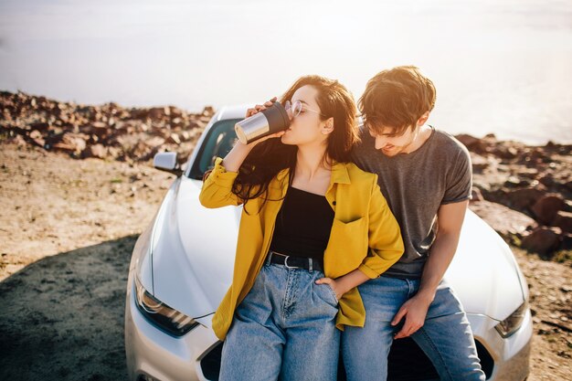 Viagens, turismo - homem e mulher bebem café ou chá perto do carro. Casal vai em aventura. Conceito de viagens de carro.