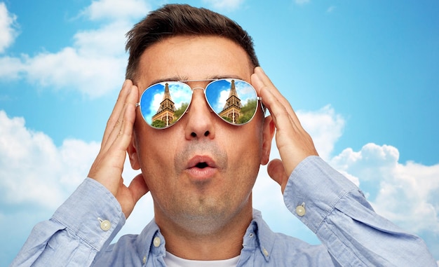 viagens, turismo, passeios, emoções e conceito de pessoas - rosto de homem em óculos de sol com reflexão da torre eiffel sobre fundo de céu azul e nuvens