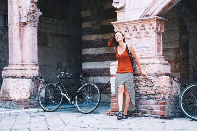 Viaja por Europa. Mujer joven con estilo en el fondo de la calle de la ciudad europea y uno de los edificios arquitectónicos históricos de Verona, Italia. Vacaciones en Europa. Arte, estilo de vida y concepto de viaje.