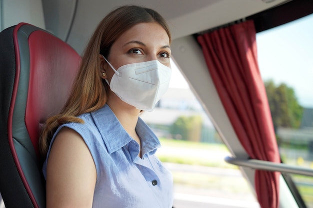 Viaja de forma segura en transporte público. Mujer joven con mascarilla protectora KN95 FFP2 mirando a través de la ventana del autobús durante su viaje.