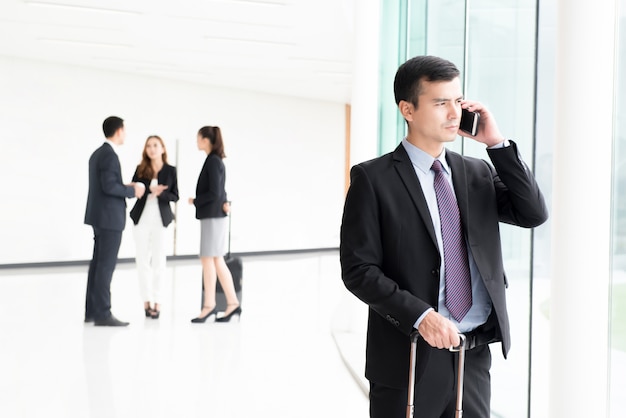 Viajando empresario llamando en el teléfono inteligente en el pasillo del edificio