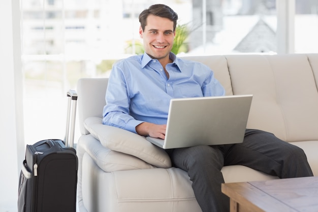 Viajando, homem negócios, usando, laptop, sentando, sofá, sorrindo, câmera