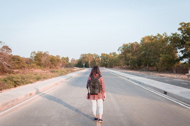 Foto viajando mulher com mochila andando na zona rural de estrada de asfalto