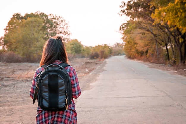 Foto viajando mulher com mochila andando na zona rural de estrada de asfalto