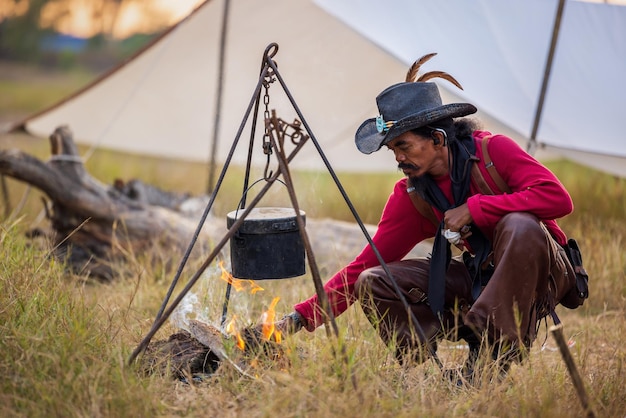 Viajando no estilo vingador, os cowboys têm acampamento ao ar livre aquecendo água quente em um acampamento, uma panela de ferro fundido cozinha em fogo aberto