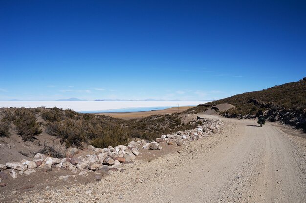 Viajante andando de bicicleta carregado de sacos de sela na estrada ao lado do deserto salgado de Uyuni, na Bolívia