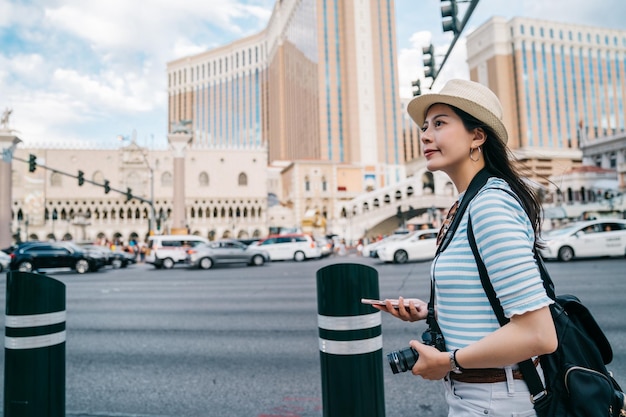 Viajante andando na rua da cidade movimentada com prédios altos ao redor da américa. jovem lente usando o aplicativo de mapa on-line, encontrando direção no centro da cidade em las vegas. mochileiro viajar sozinho.