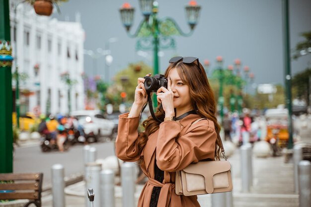 Viajante asiática com cabelos castanhos longos tirando fotos com sua câmera enquanto está de pé nas calçadas