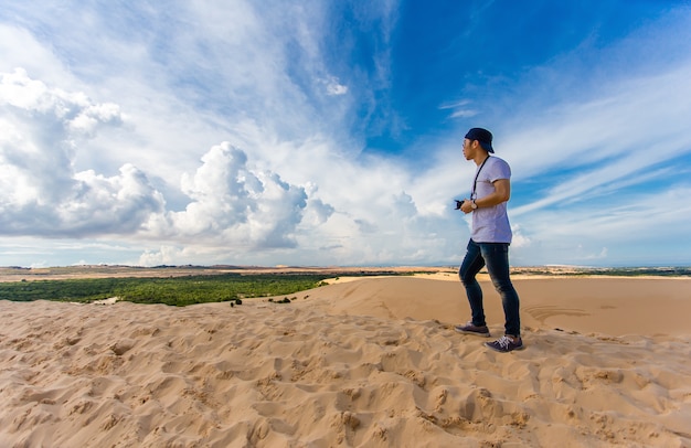 Viajante asiático novo que toma a foto com a câmera mirrorless nas dunas de areia brancas Mui Ne