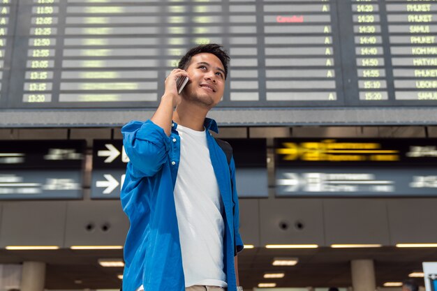 Viajante asiático verificando a tela de informações de voo em um aeroporto moderno