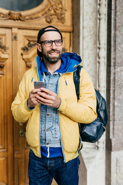 Viajante barbudo com sorriso encantador, vestindo roupas da moda e segurando a mochila