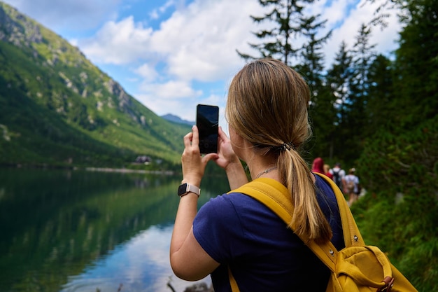 Viajante caminhando em um lago de montanha tirando fotos com um smartphone
