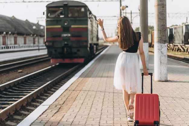 Viajante com uma mala vermelha com saia branca esperando o trem na estação ferroviária