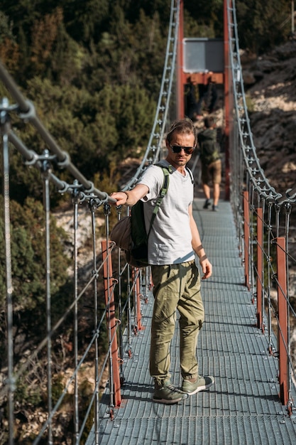 Viajante com uma mochila nas montanhas. Um homem de meia idade está em uma ponte suspensa.