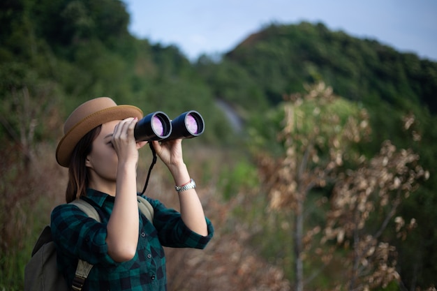 Foto viajante da mulher de ásia com binóculos e na floresta, conceito do curso.