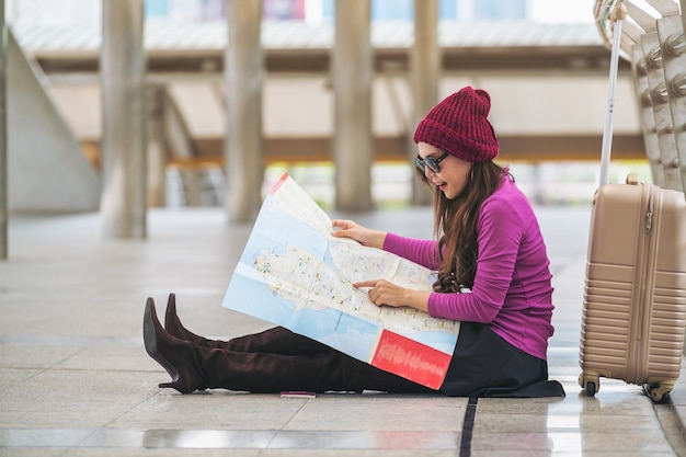 Viajante da mulher que olha o mapa do curso na passagem do aeroporto com saco ou bagagem.