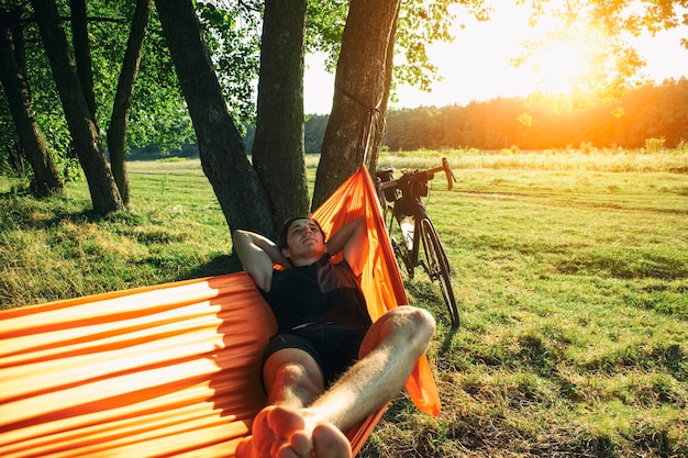 Viajante de bicicleta descansando na rede após um longo dia andando de bicicleta embalado por malas ao pôr do sol
