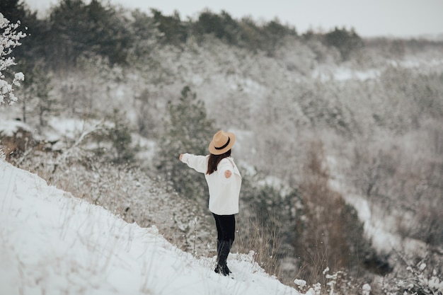 Viajante de garota feliz com as mãos ao alto, de pé no topo da montanha e olhando a bela paisagem de inverno nevado.