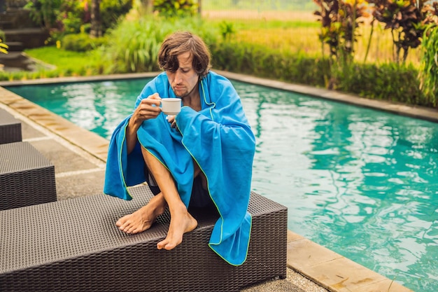 Viajante de homem doente. O homem pegou um resfriado nas férias, senta-se triste na piscina tomando chá e assoa o nariz em um guardanapo. Seu filho está saudável e nadando na piscina. Conceito de seguro de viagem