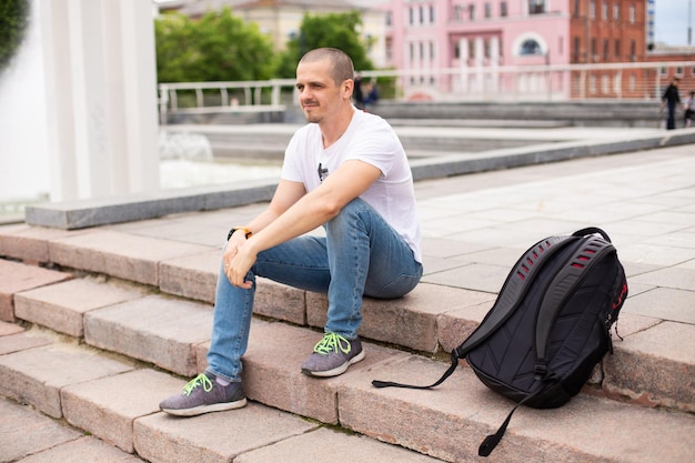 Viajante de homem sentado na escada e relaxando no parque urbano. Mochila para viajar nas escadas