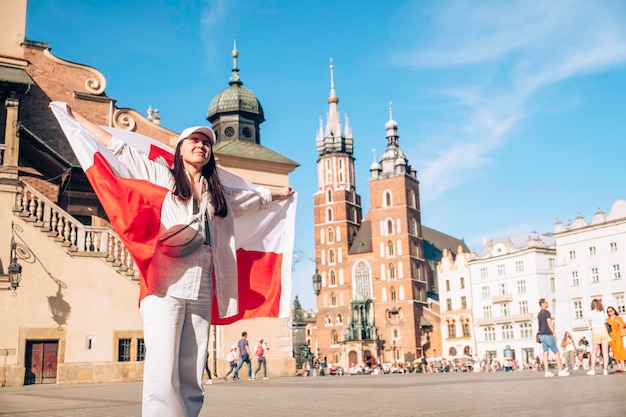 Viajante de mulher coberta com bandeira da polônia no centro da cidade de Cracóvia