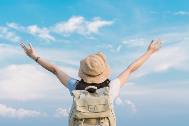 Viajante de mulher com mochila segurando o chapéu e olhando para o céu azul, conceito de viagens, espaço para texto e momento atmosférico