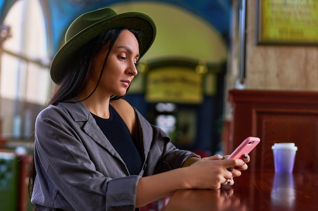 Viajante de mulher elegante elegante fofo atraente hipster usando um telefone durante um descanso em uma cafeteria