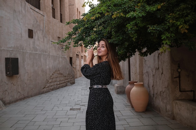 Viajante de mulher feliz com vestido preto, caminhando pelas ruas de uma antiga cidade ou vila árabe no meio do deserto. conceito de turismo e aventuras em al seef dubai