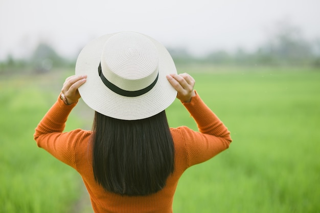 Viajante de mulher segurando o chapéu e olhando para o campo verde