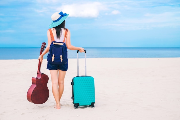 Viajante de mulher tem uma bagagem e guitarra em pé na praia