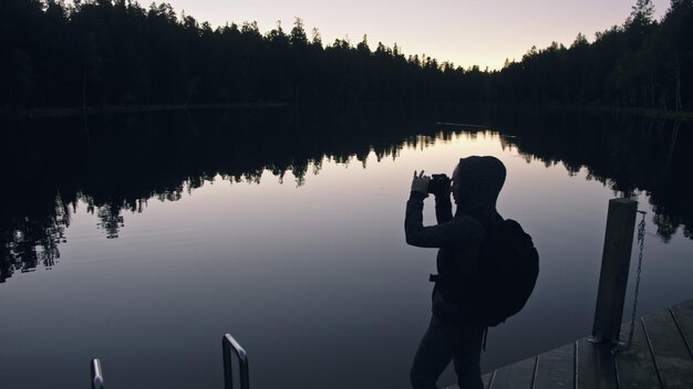 Viajante de silhueta fotografando a vista panorâmica no rio da floresta