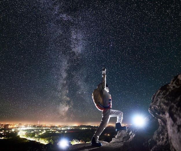 Viajante do espaço em pé na montanha rochosa sob o céu noturno com estrelas