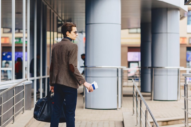 Viajante elegante em jaqueta com passaporte e bilhetes em contexto urbano