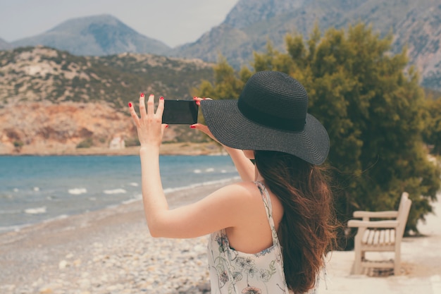 Viajante fêmea que fotografa em vistas naturais bonitas do smartphone do mar e das montanhas na ilha de Creta.