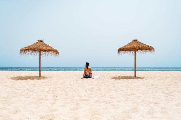 Viajante feminina sentada na areia perto do oceano